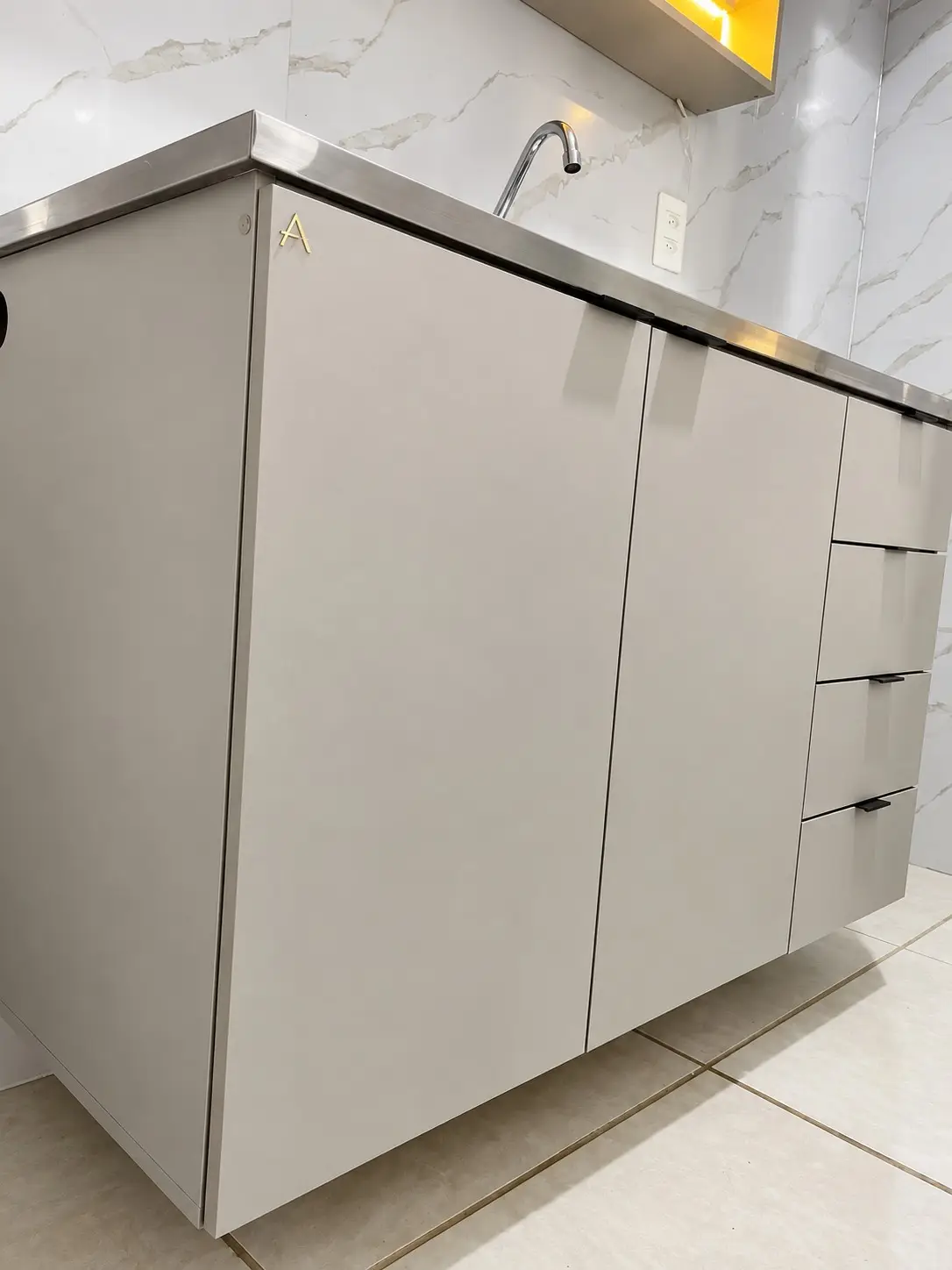 Área de serviço planejada sob medida em laca fendi com bancada de inox e a letra A em latão
