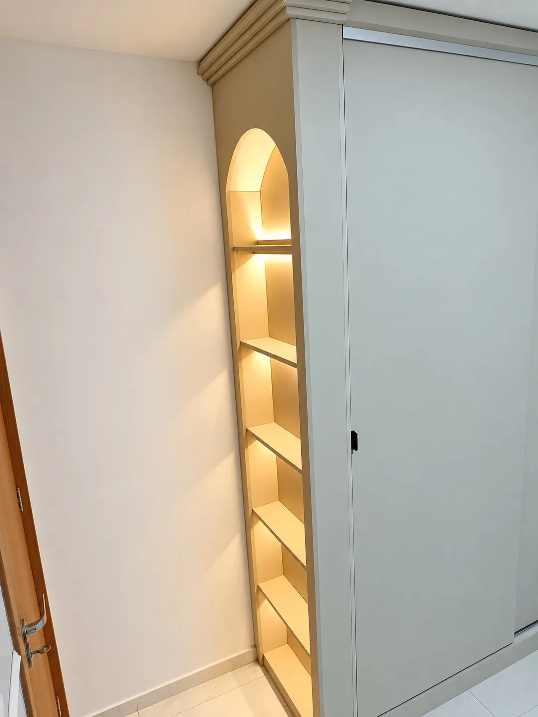 Nicho arqueado com prateleiras e iluminação embutida na lateral do guarda-roupa planejado