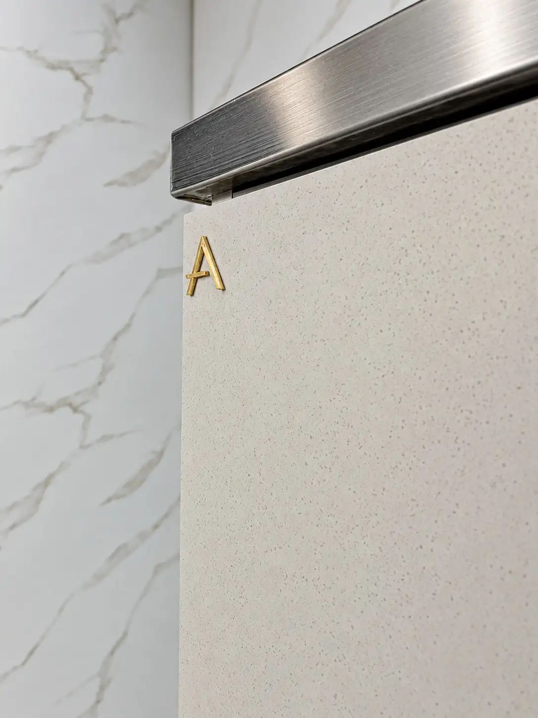 Detalhe de porta em laca com a letra A em latão embutida, sob perfil de inox escovado — acabamento Alfa Projetados