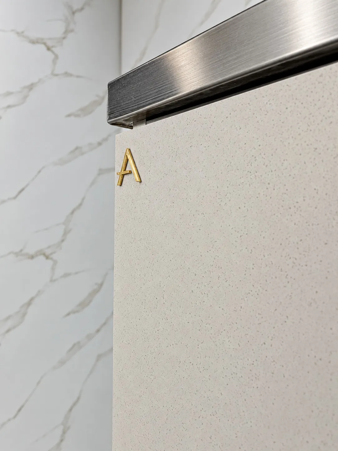 Macro do encontro entre a porta em laca fendi e o perfil de inox escovado, com a letra A em latão